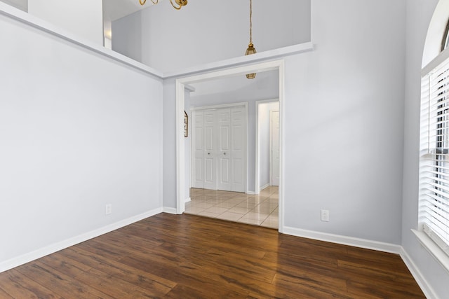 empty room featuring dark wood-type flooring, a high ceiling, and a chandelier