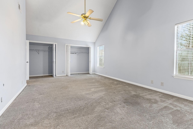 unfurnished bedroom with carpet floors, two closets, high vaulted ceiling, and ceiling fan