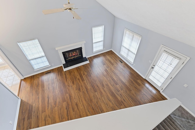 unfurnished living room featuring ceiling fan, a towering ceiling, and wood-type flooring