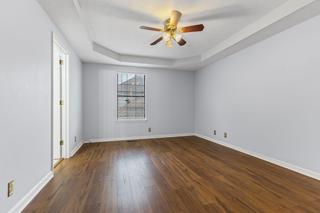 empty room featuring a textured ceiling, ceiling fan, dark wood-type flooring, and a tray ceiling