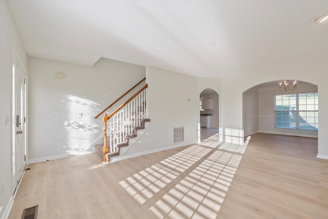 unfurnished living room with light wood-type flooring and a notable chandelier