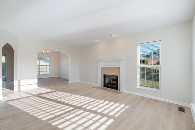 unfurnished living room featuring a tile fireplace, light hardwood / wood-style flooring, and an inviting chandelier