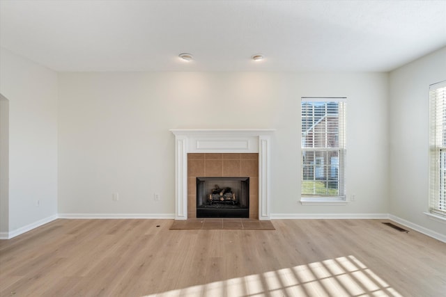 unfurnished living room with a tile fireplace, plenty of natural light, and light hardwood / wood-style floors