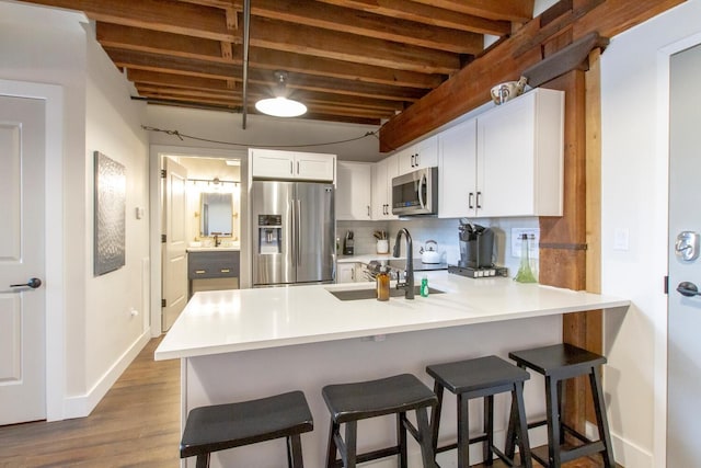 kitchen with white cabinets, sink, beamed ceiling, kitchen peninsula, and stainless steel appliances