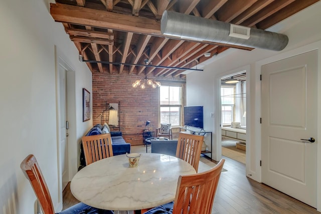 dining area with hardwood / wood-style floors, brick wall, and an inviting chandelier