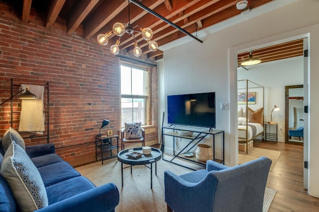 living room with a chandelier, light hardwood / wood-style flooring, beamed ceiling, and brick wall