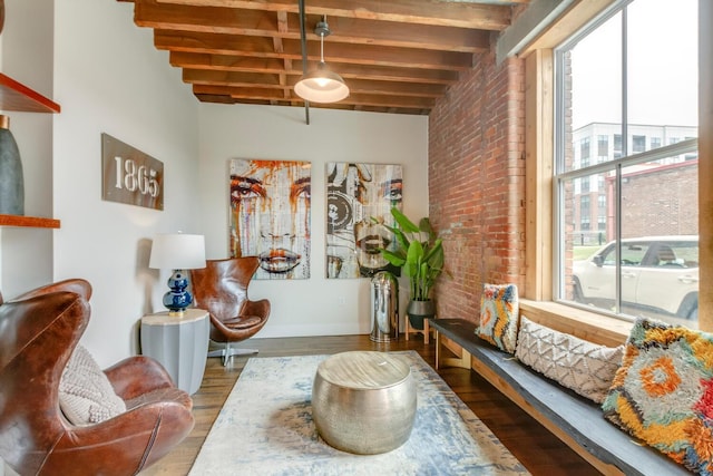 sitting room with hardwood / wood-style floors, beam ceiling, and brick wall