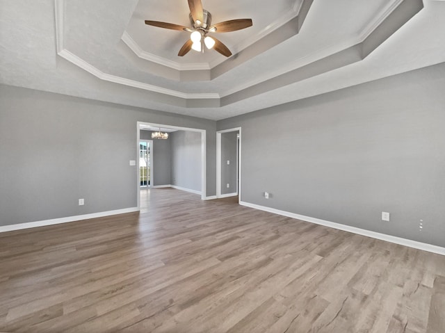 unfurnished room featuring ceiling fan with notable chandelier, a raised ceiling, light wood-type flooring, and crown molding