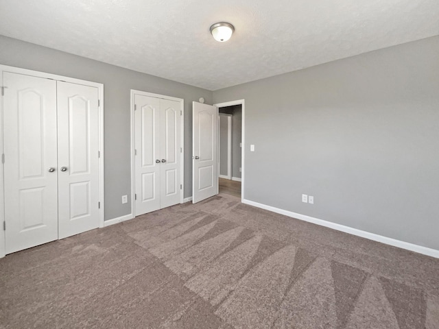 unfurnished bedroom featuring carpet, a textured ceiling, and multiple closets