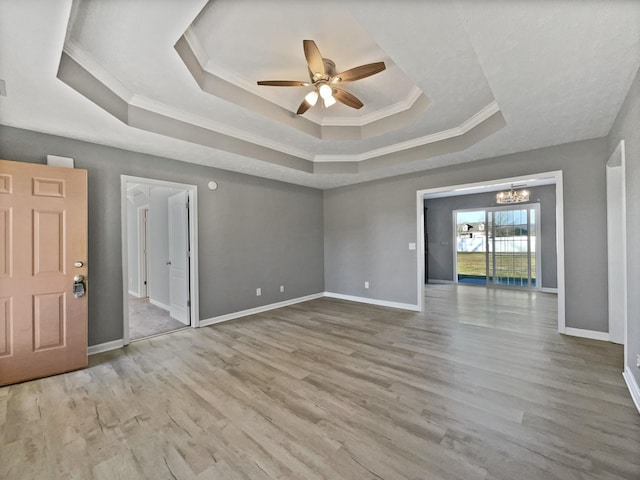 interior space featuring ceiling fan with notable chandelier, light hardwood / wood-style floors, a raised ceiling, and ornamental molding