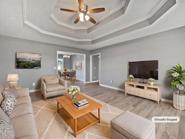 living room with a raised ceiling, crown molding, light hardwood / wood-style floors, and ceiling fan with notable chandelier