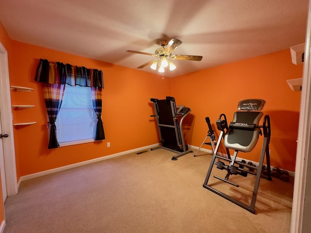 exercise area featuring ceiling fan, light colored carpet, and a textured ceiling