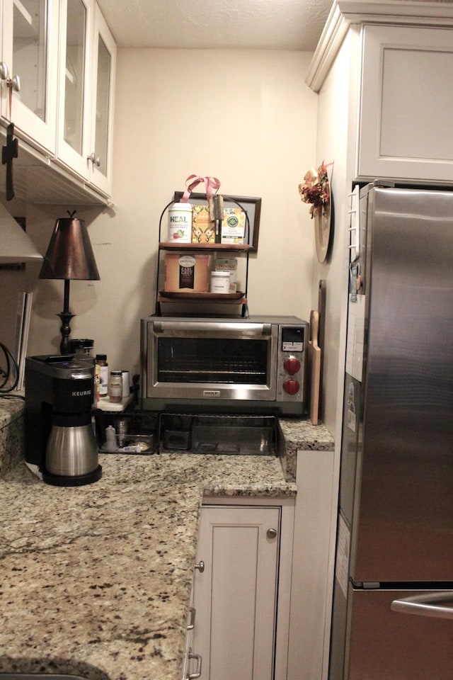 kitchen featuring white cabinetry, stainless steel fridge, and light stone counters