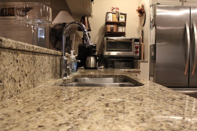 kitchen featuring decorative backsplash, stainless steel fridge, sink, and light stone counters