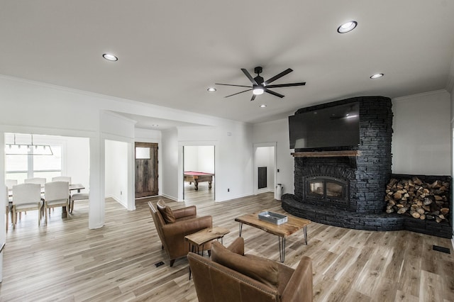 living room with ornamental molding, ceiling fan, light hardwood / wood-style floors, and a stone fireplace