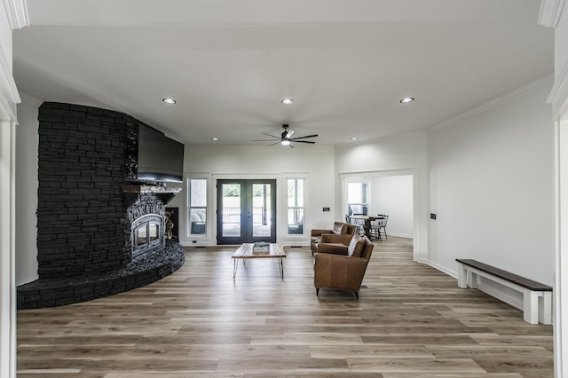 living room with light hardwood / wood-style flooring, french doors, ceiling fan, ornamental molding, and a stone fireplace