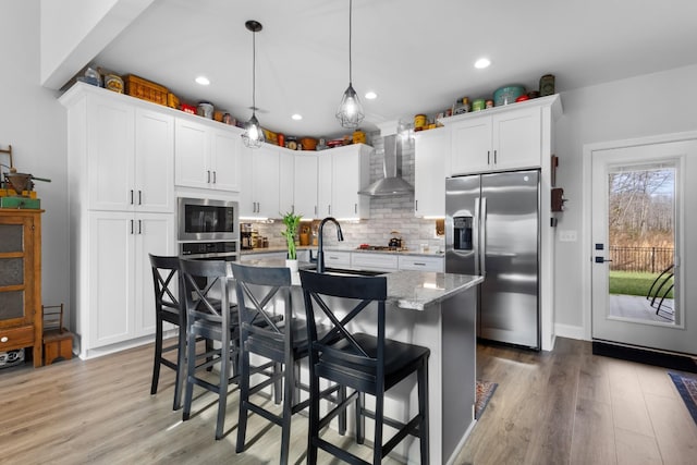 kitchen with built in microwave, hanging light fixtures, wall chimney range hood, stainless steel fridge with ice dispenser, and an island with sink