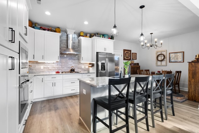 kitchen featuring a kitchen breakfast bar, wall chimney range hood, decorative light fixtures, a kitchen island, and stainless steel appliances