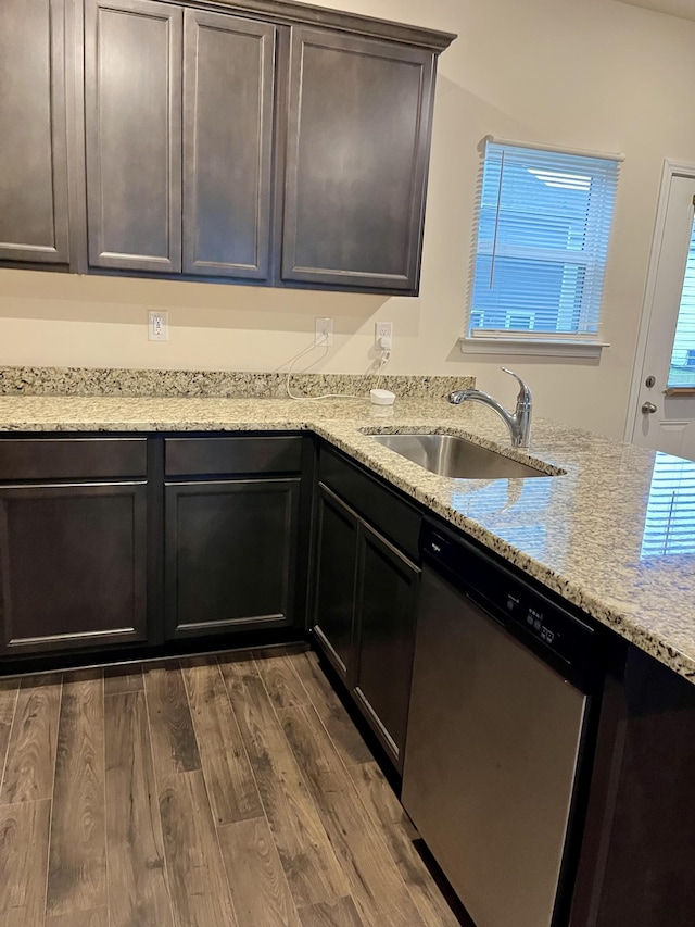 kitchen featuring light stone counters, stainless steel dishwasher, dark brown cabinetry, sink, and wood-type flooring