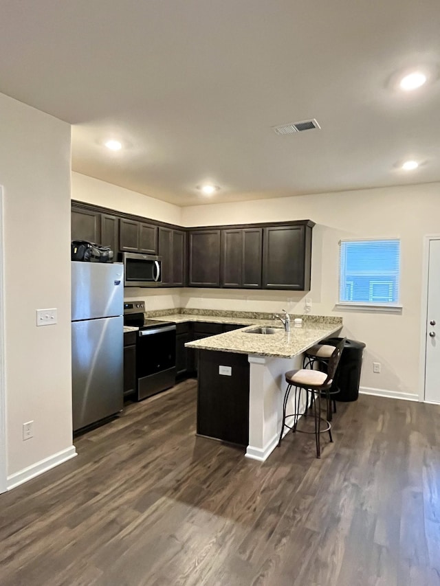 kitchen with kitchen peninsula, appliances with stainless steel finishes, light stone counters, dark wood-type flooring, and a breakfast bar area