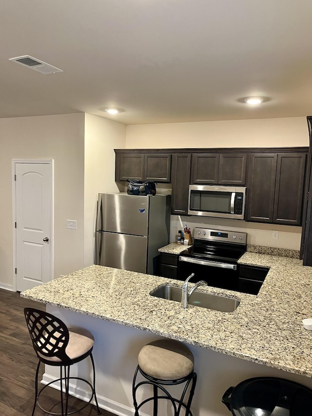 kitchen with a kitchen bar, light stone counters, sink, and appliances with stainless steel finishes