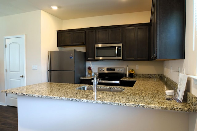 kitchen with light stone counters, dark brown cabinetry, appliances with stainless steel finishes, and a peninsula