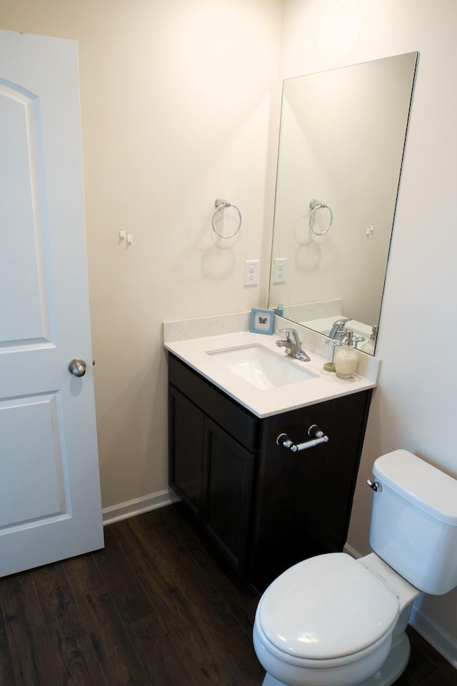 bathroom with vanity, toilet, wood finished floors, and baseboards