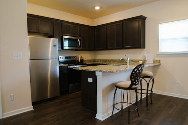 kitchen with a sink, dark brown cabinetry, light stone counters, and stainless steel appliances