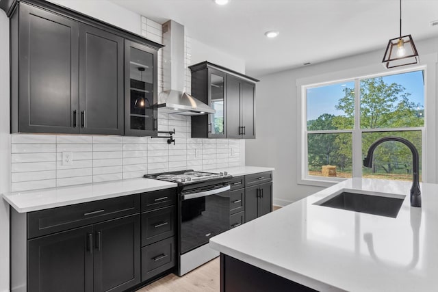 kitchen with tasteful backsplash, wall chimney exhaust hood, stainless steel range, sink, and light hardwood / wood-style flooring