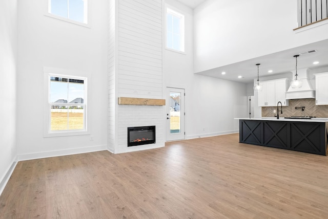 unfurnished living room featuring a fireplace, a towering ceiling, light hardwood / wood-style floors, and sink