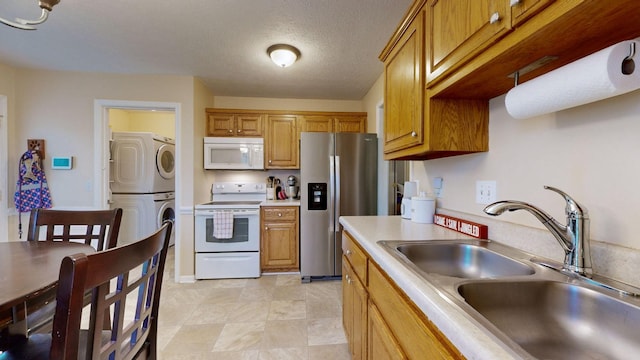 kitchen featuring a textured ceiling, stacked washer and dryer, white appliances, and sink