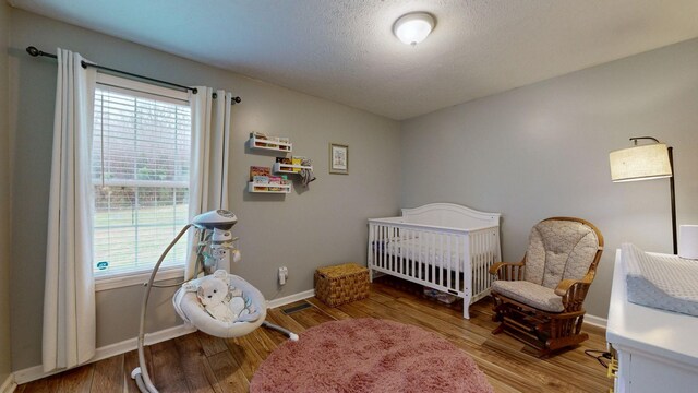 bedroom with a crib, wood-type flooring, and multiple windows