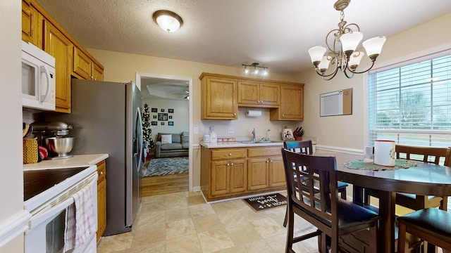 kitchen featuring sink, an inviting chandelier, a textured ceiling, decorative light fixtures, and white appliances