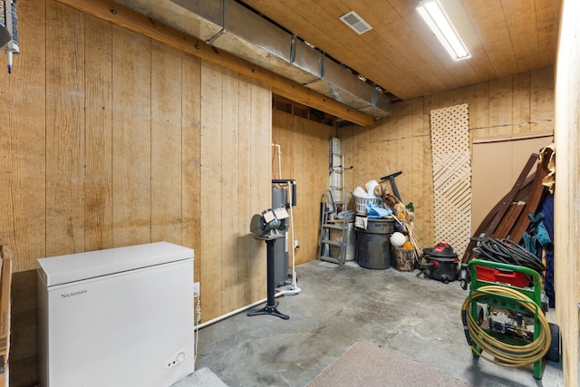 basement featuring wooden walls and fridge