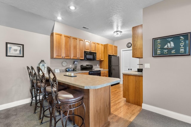 kitchen featuring kitchen peninsula, a textured ceiling, light colored carpet, black appliances, and a breakfast bar area