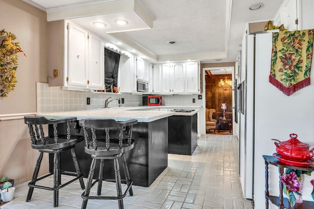 kitchen featuring a kitchen breakfast bar, kitchen peninsula, tasteful backsplash, white fridge, and white cabinetry