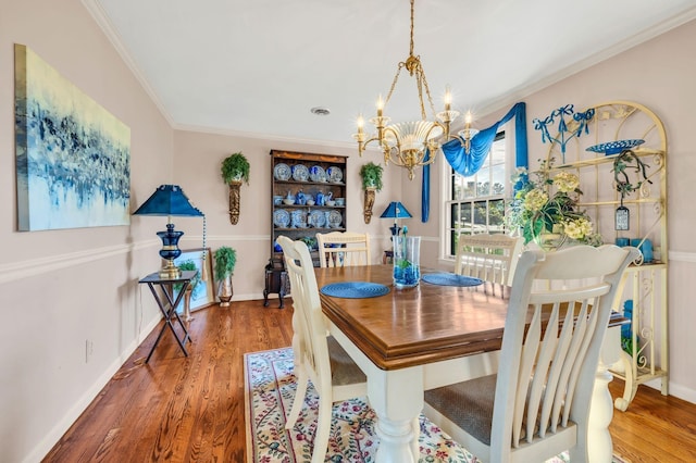 dining space with wood-type flooring, ornamental molding, and a notable chandelier