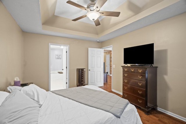 bedroom with hardwood / wood-style flooring, ceiling fan, ensuite bath, and a tray ceiling