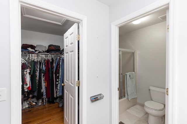 bathroom with hardwood / wood-style flooring, combined bath / shower with glass door, and toilet