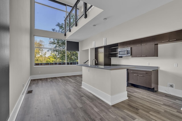 kitchen featuring light wood-type flooring, dark brown cabinetry, an island with sink, and hanging light fixtures