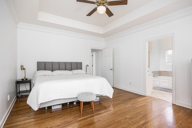 bedroom featuring hardwood / wood-style floors, crown molding, ceiling fan, connected bathroom, and a tray ceiling