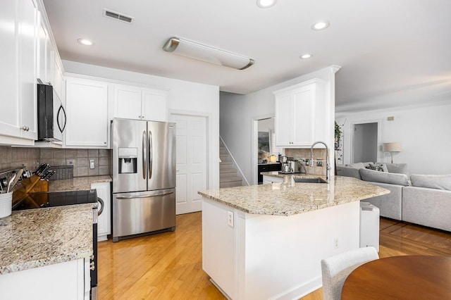 kitchen featuring white cabinets, decorative backsplash, stainless steel fridge, light stone countertops, and range