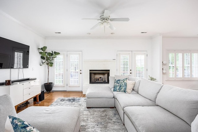 living room featuring crown molding, a fireplace, ceiling fan, and light hardwood / wood-style flooring