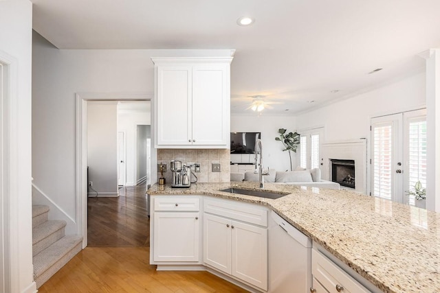 kitchen with decorative backsplash, light wood-type flooring, white cabinets, light stone counters, and dishwasher