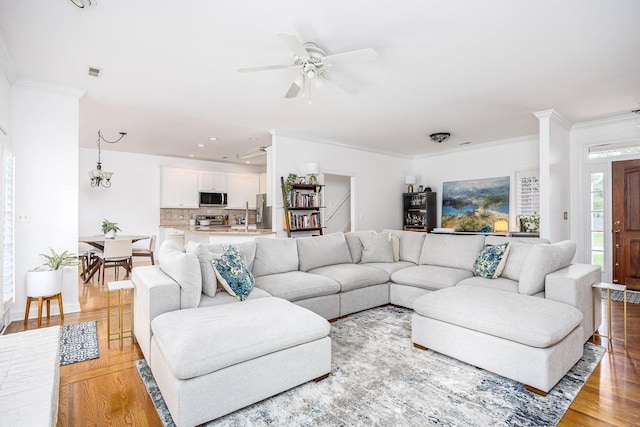 living room with crown molding, ceiling fan with notable chandelier, and light wood-type flooring