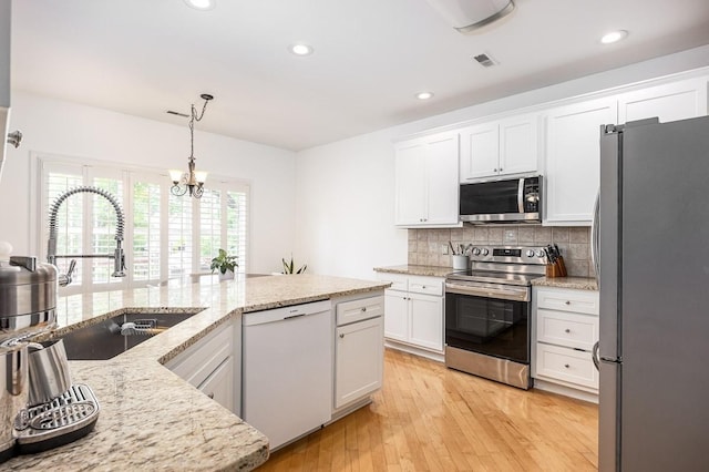 kitchen with light stone countertops, stainless steel appliances, sink, white cabinetry, and hanging light fixtures