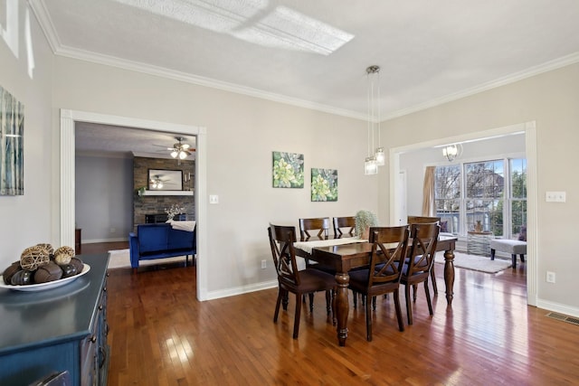 dining room featuring ceiling fan with notable chandelier, a stone fireplace, crown molding, and dark hardwood / wood-style floors