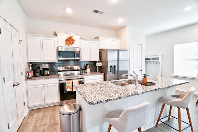 kitchen featuring light stone countertops, appliances with stainless steel finishes, a kitchen island with sink, sink, and white cabinets