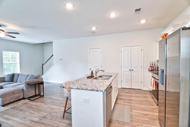 kitchen featuring white cabinets, sink, an island with sink, light hardwood / wood-style floors, and a breakfast bar area