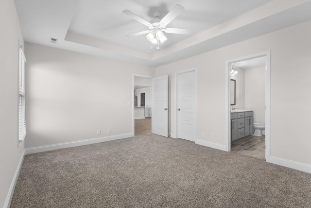 unfurnished bedroom with ensuite bathroom, ceiling fan, a tray ceiling, and light carpet